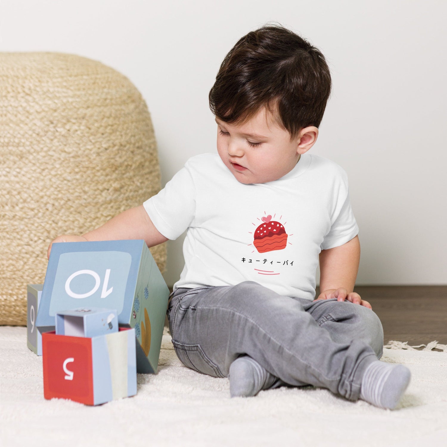 a baby who is wearing a Japanese letter t-shirt is sitting down on the floor